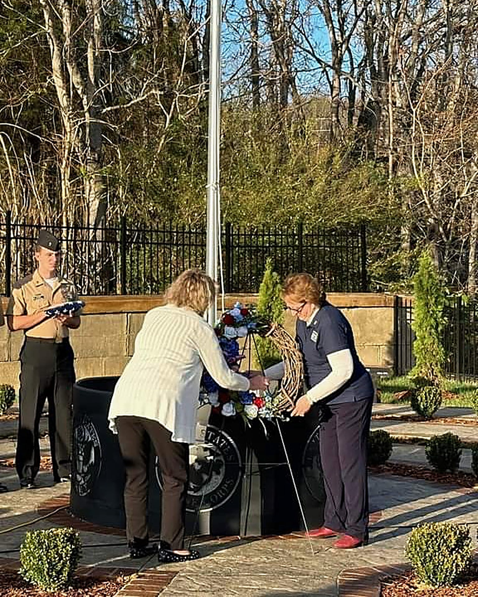 Joyce Crosswhite placing a wreath at the Sullivan County Veterans Memorial Park ceremony, with a Marine holding a folded flag